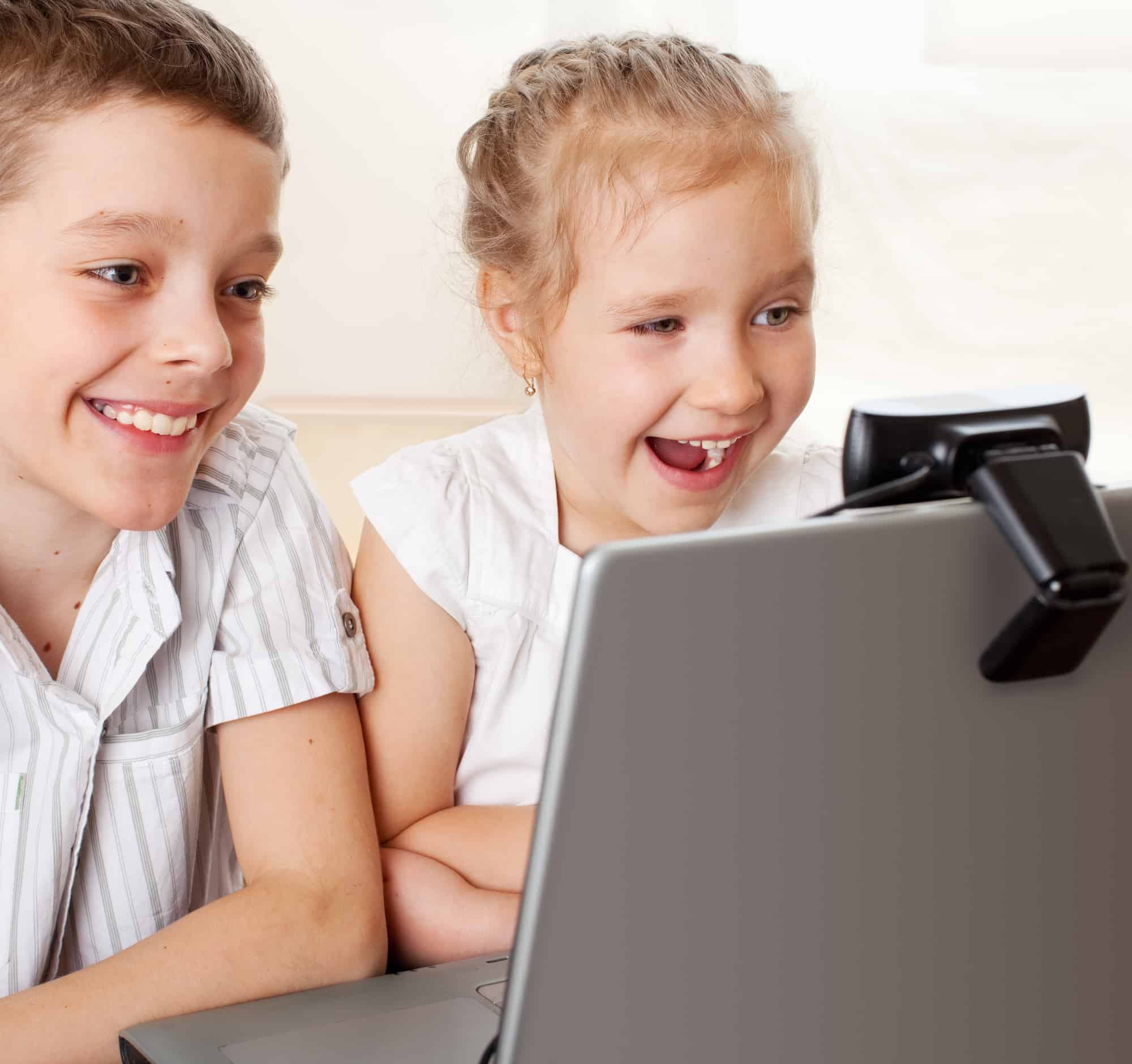 Two children smiling and laughing on the computer as they face time.