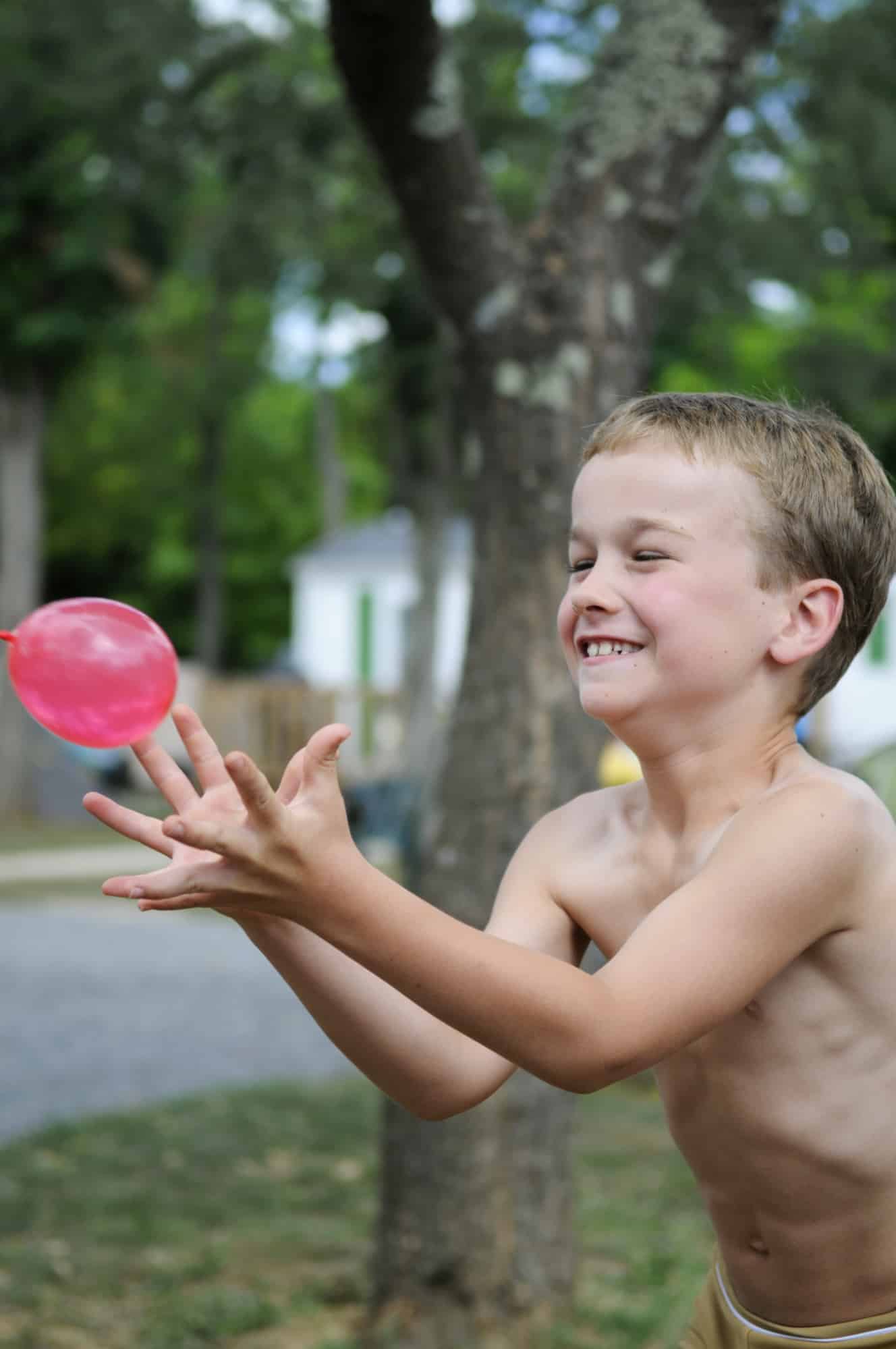 Little boy smiling while catching a water balloon.