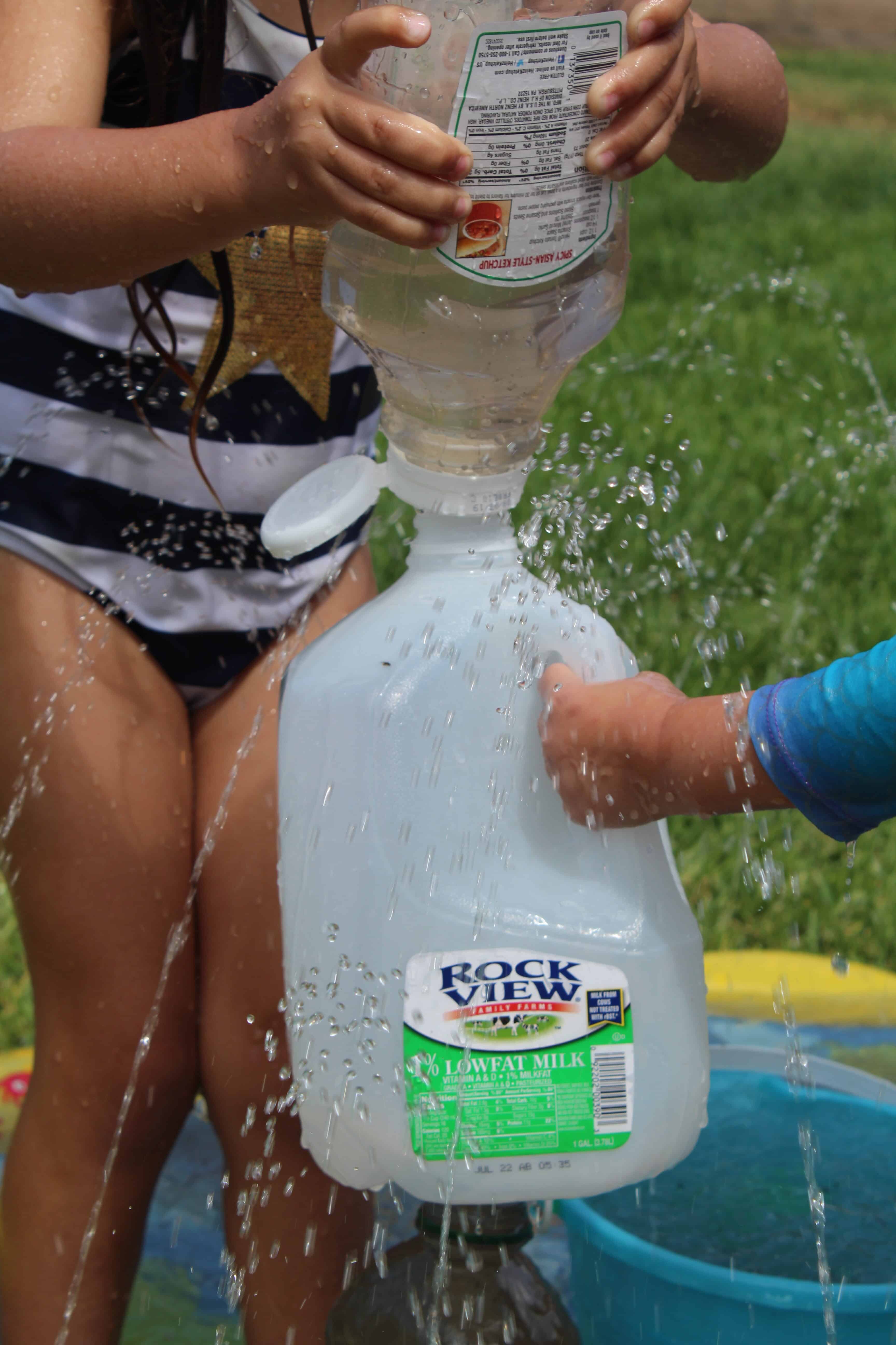 little girl using a ketchup bottle to squirt water into a milk jug