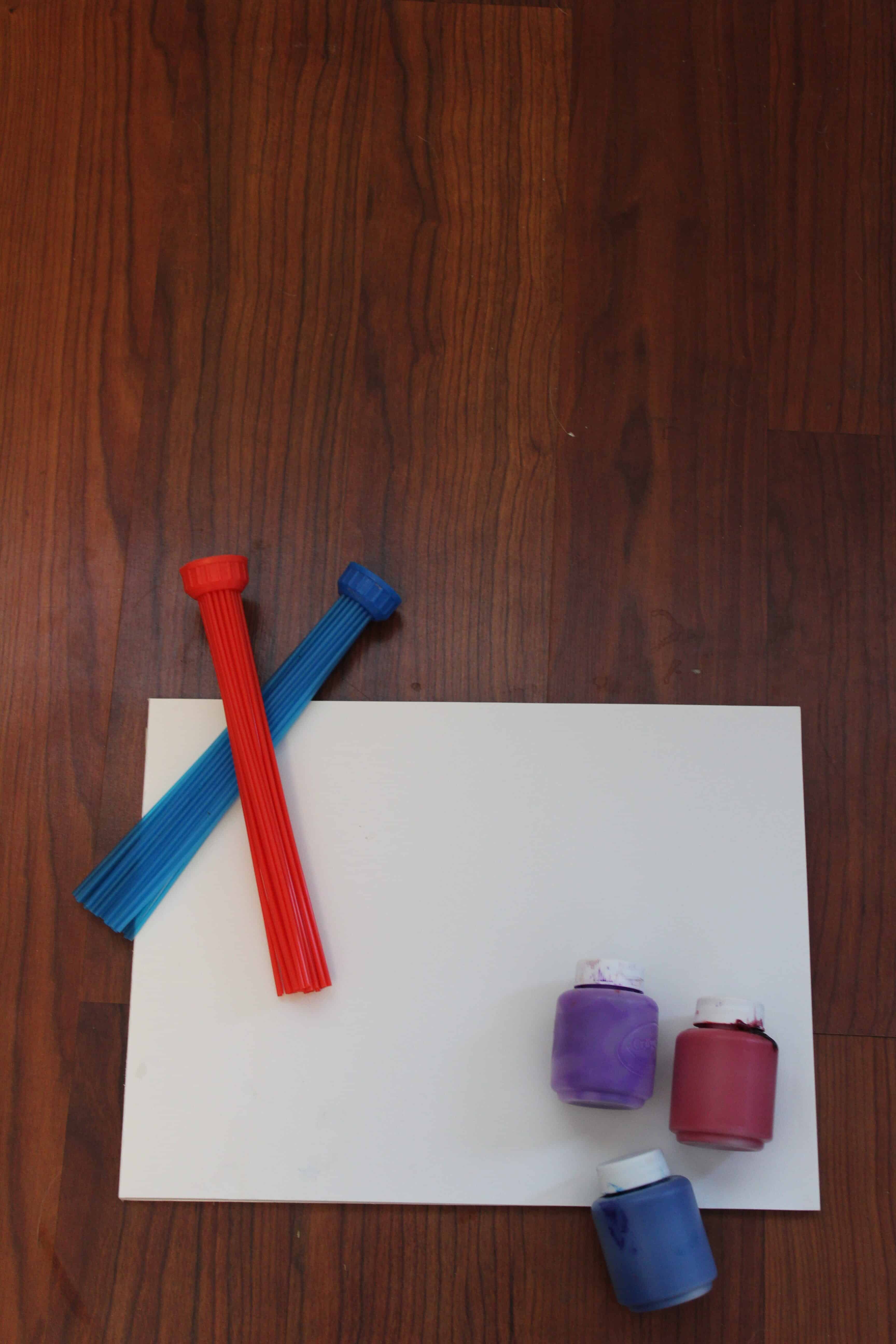 Bunch a balloons fast filler being used as a paintbrush resting against a white sheet of paper. Blue, purple and red paint in bottle.