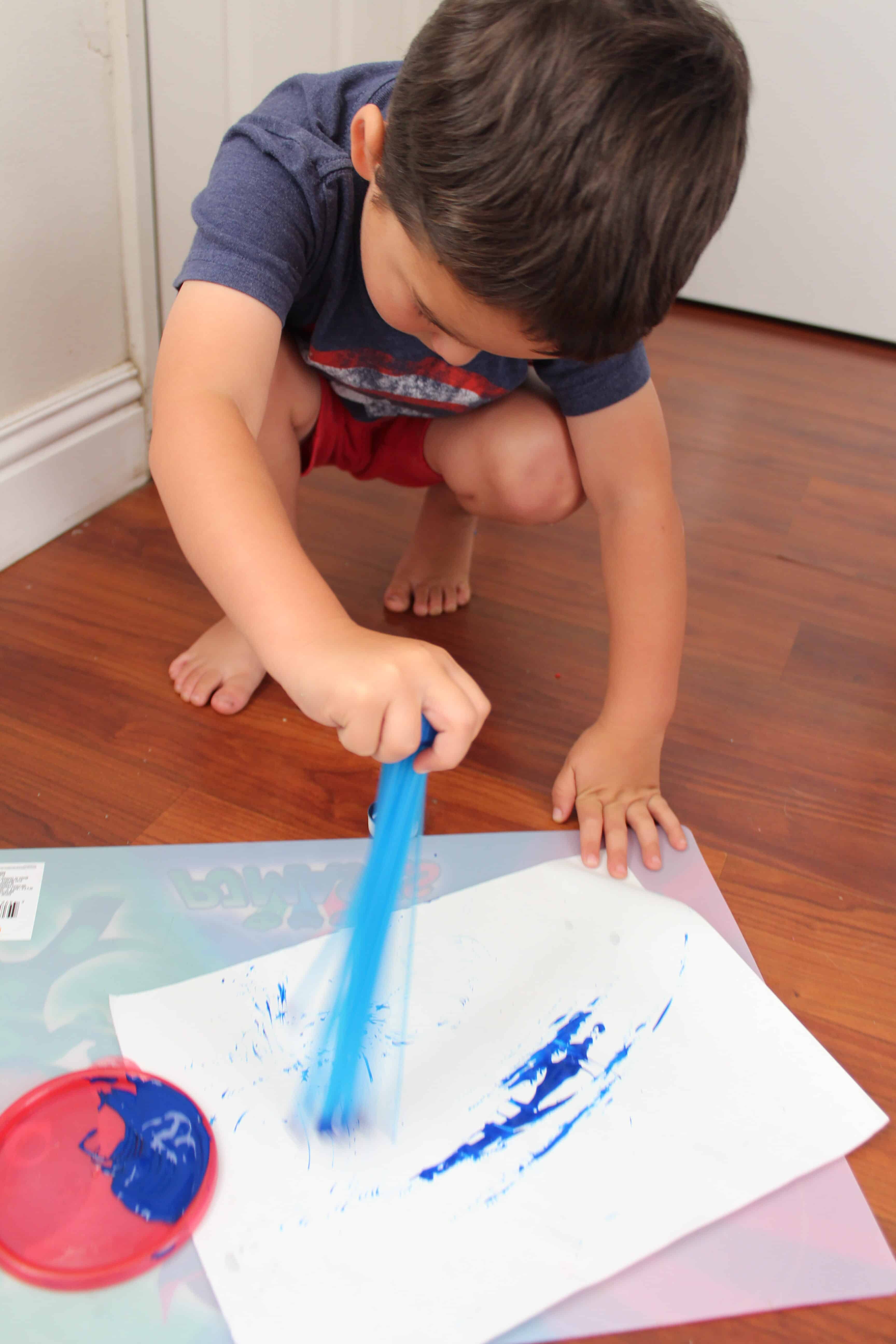 Toddler crouched using the bunch a balloons at the paint brush. 