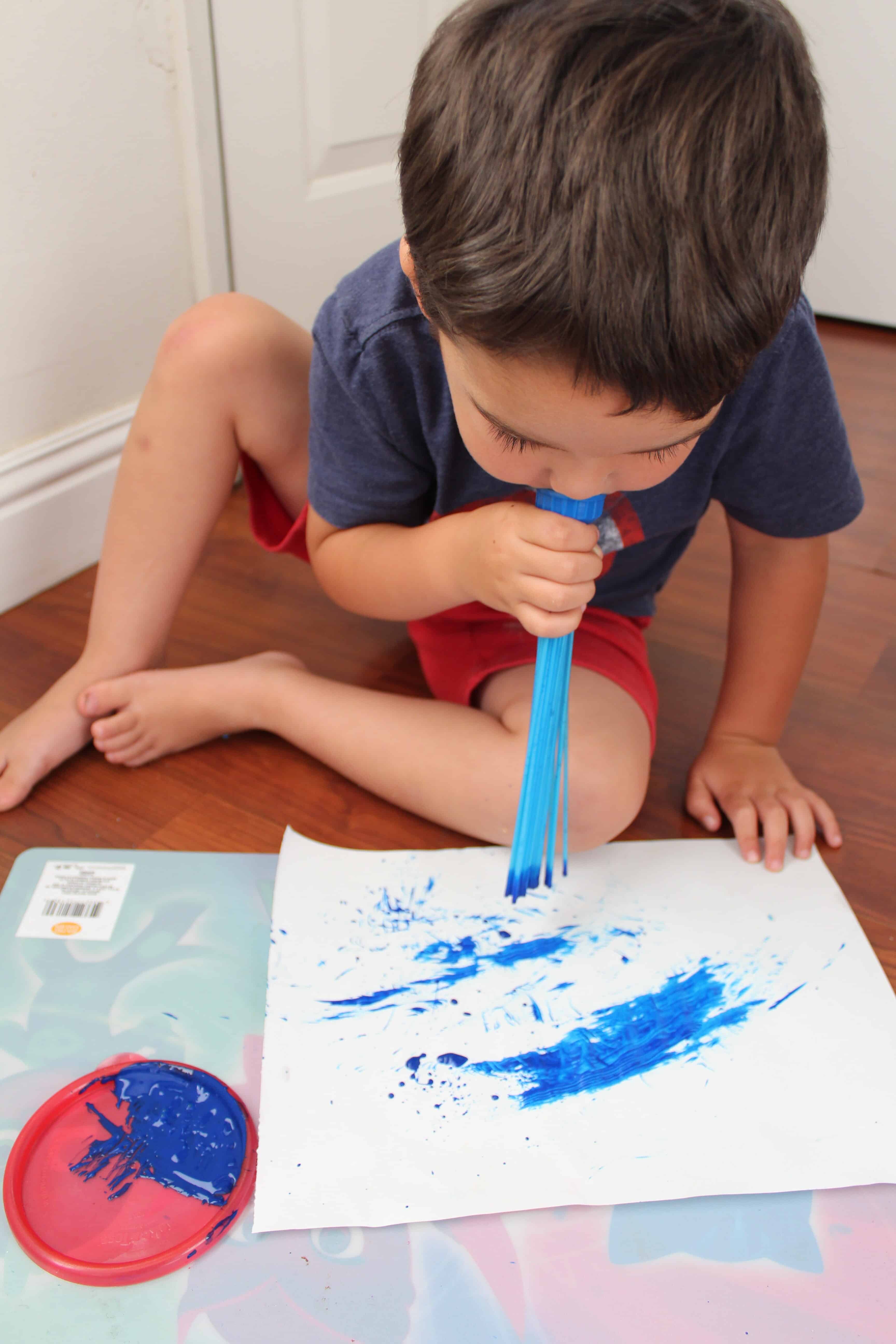 Toddler blowing on the bunch a balloons maker end cap to push pain onto the paper. 