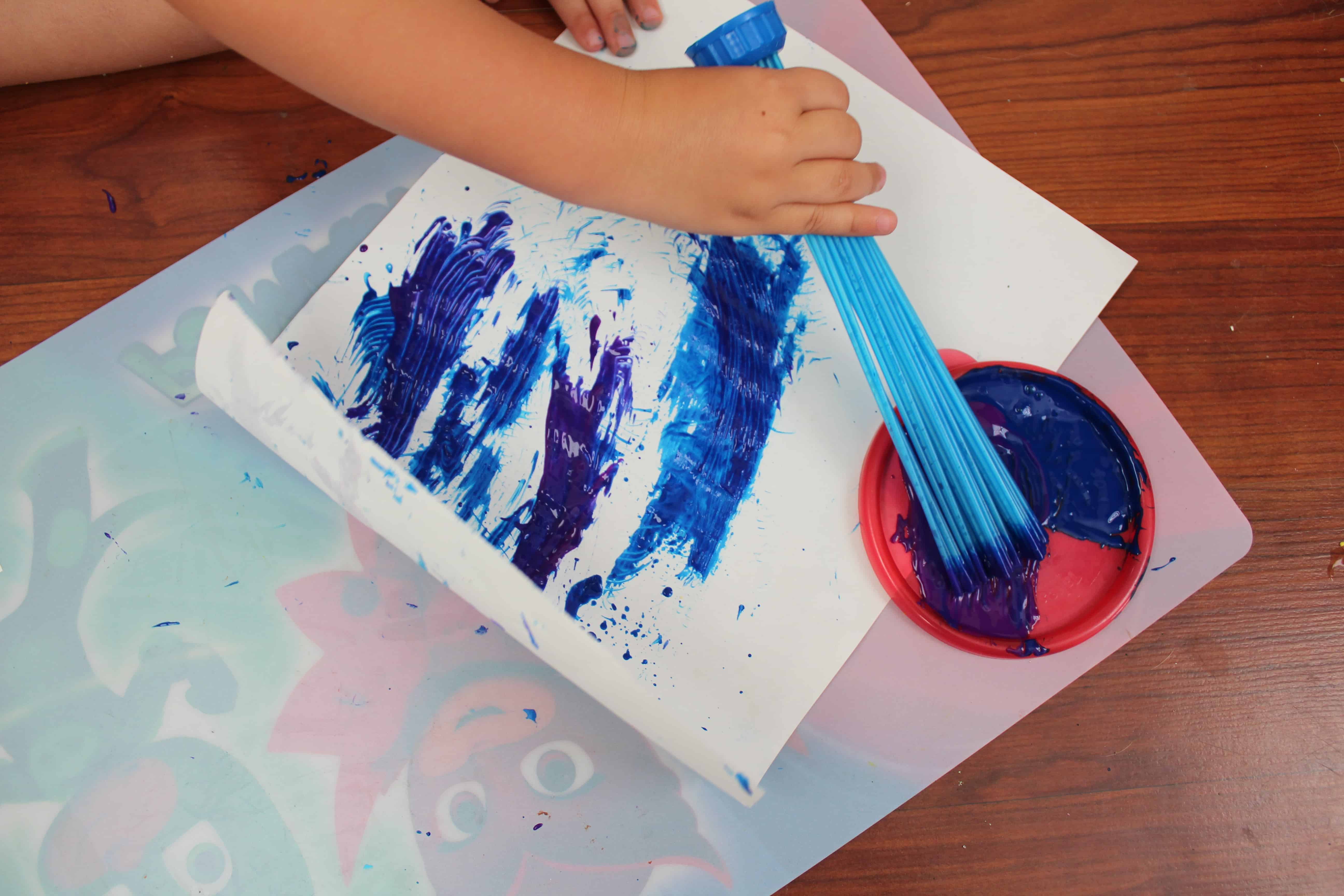 Bunch a balloons paint brush being used to paint blue on a white sheet of paper. 