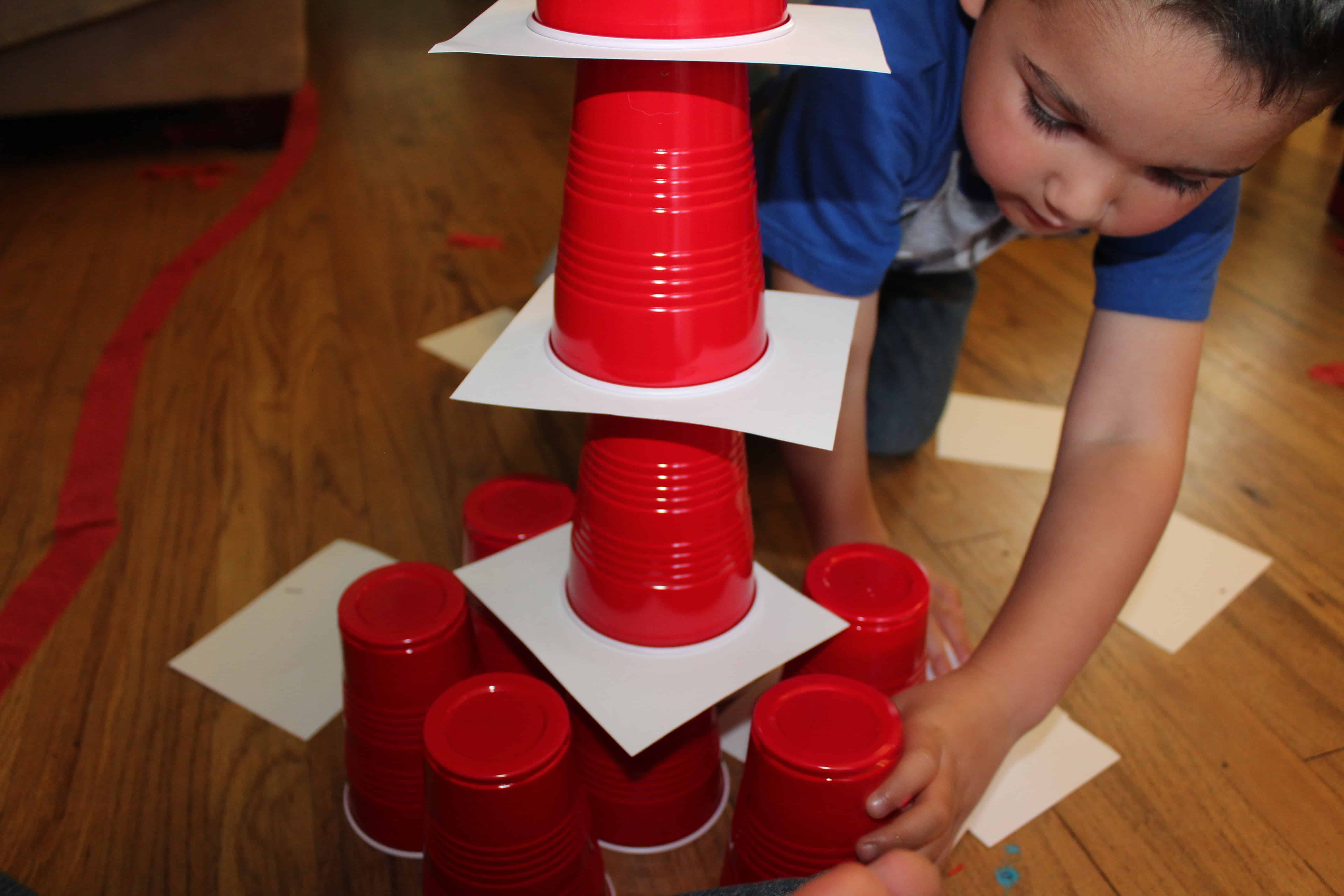 preschooler building a tower with red solo cups and white paper