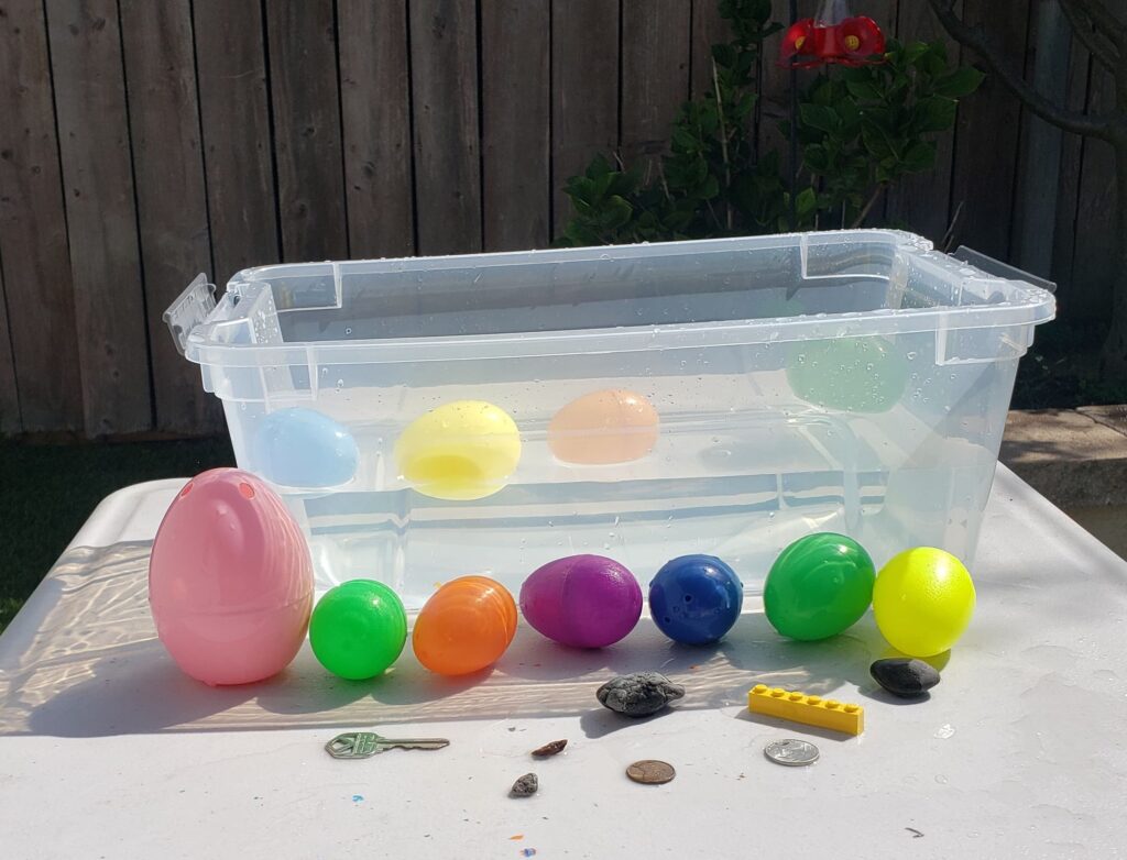 Plastic tub filled with water, plastic easter eggs and household items to use to play Sink or Float