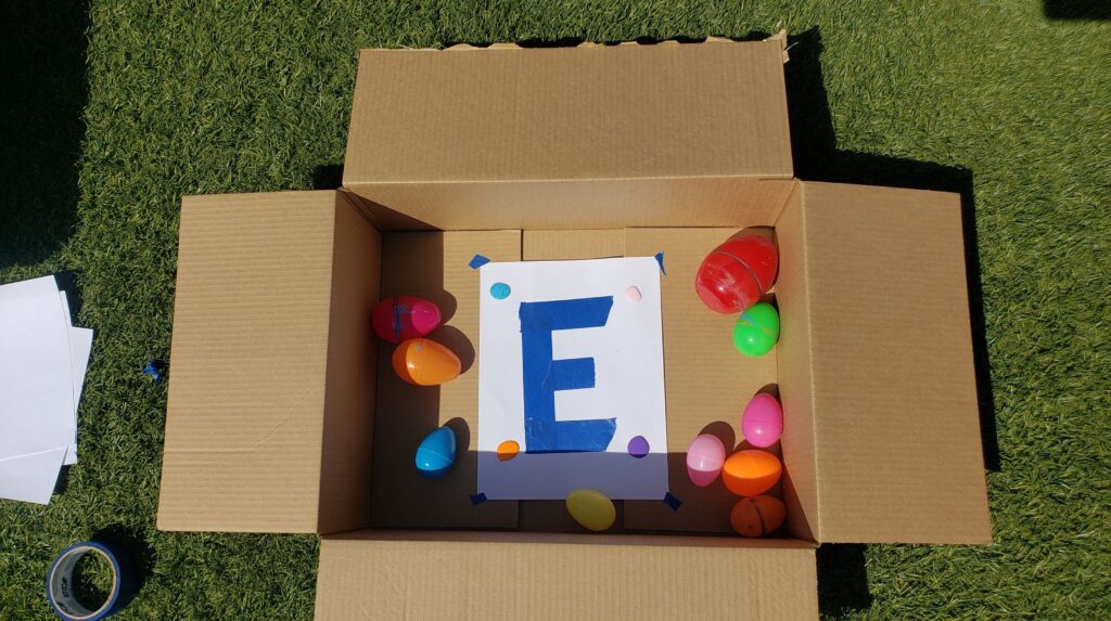 Cardboard box with a paper inside. Plastic Easter eggs and paint are inside as well to create egg roll art!