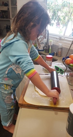 Little girl using a rolling pin to flatten salt and flour mixture.