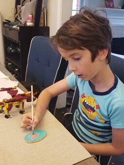 Child painting a dough ornament with pink petals. 