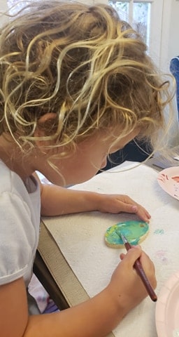 Toddler painting an egg ornament with bright colors. 