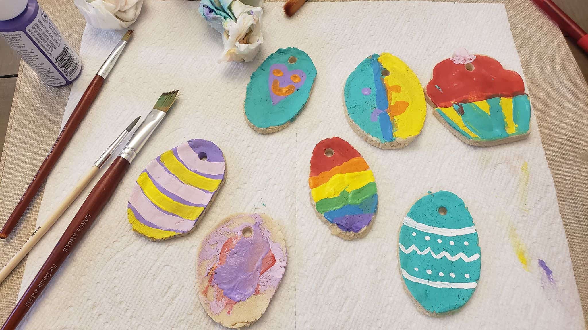 Different dough ornaments painted bright colors drying on a paper ornaments. 