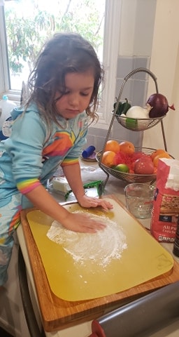 Little girl dusting a cutting board with flour to work the dough on. 