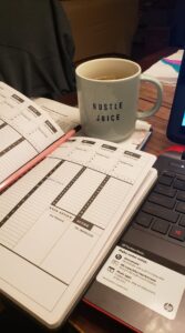 a planner and a cup of tea in a mug that says "hustle juice"