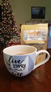 a cup of tea in a cup that says "live the story you want to tell," in front of a bag of loose tea called heartlight
