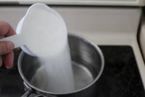 pouring sugar into homemade snow cone syrup recipe