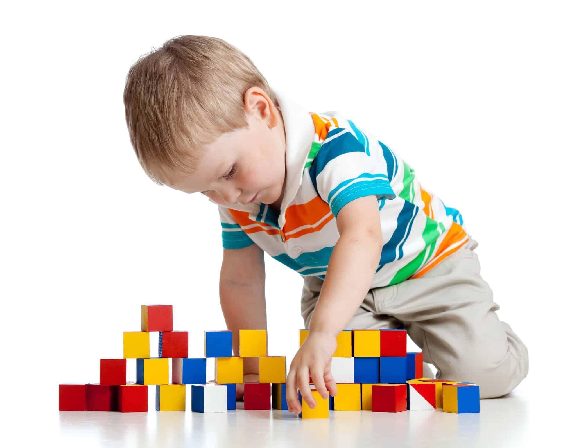 A little boy in a striped shirt building a wall with colorful square blocks