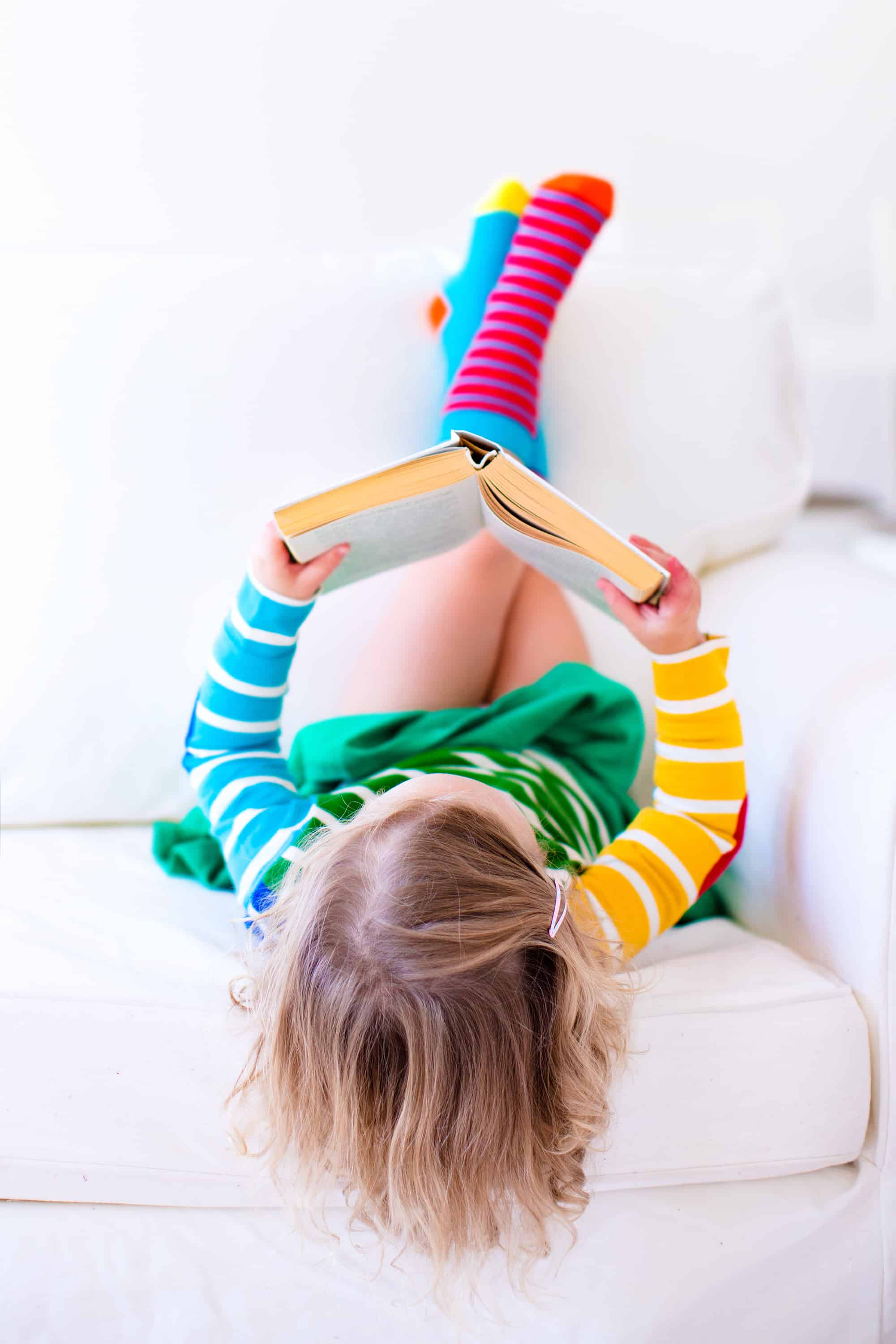 preschool girl reading upside down on the couch