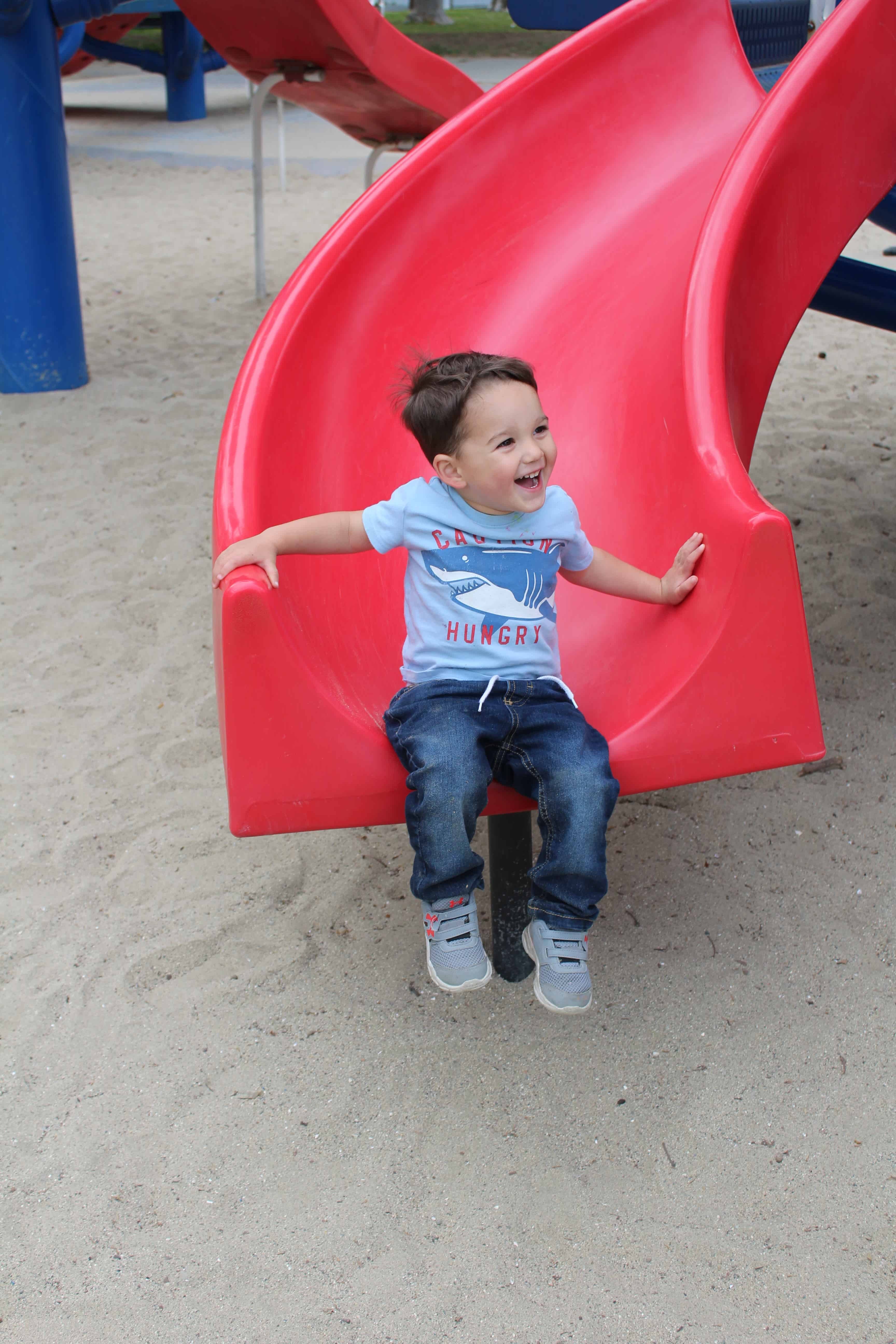 A preschool boy sliding down a red slide with a big smile on his face