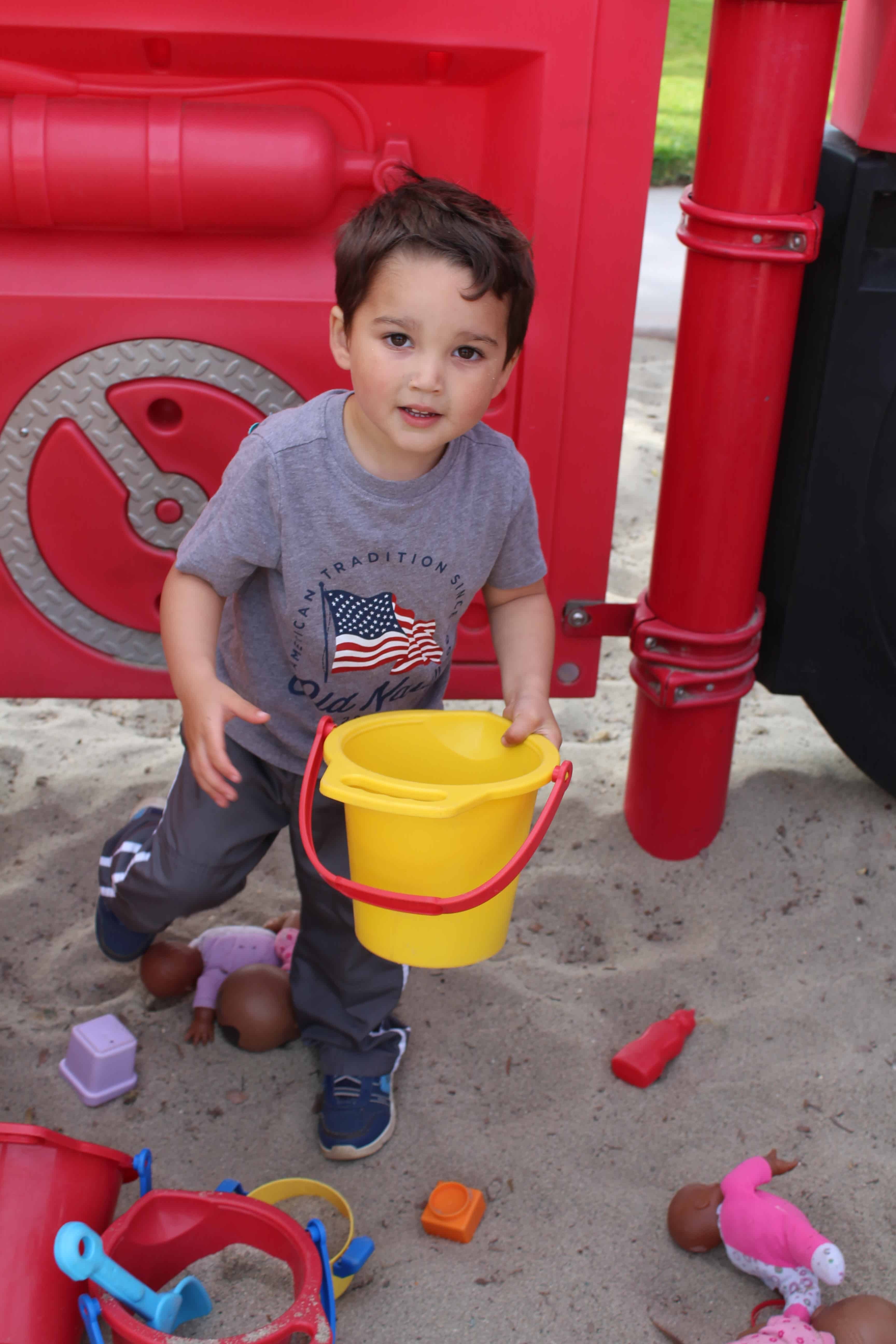 a little boy playing in the sand with a yellow bucket