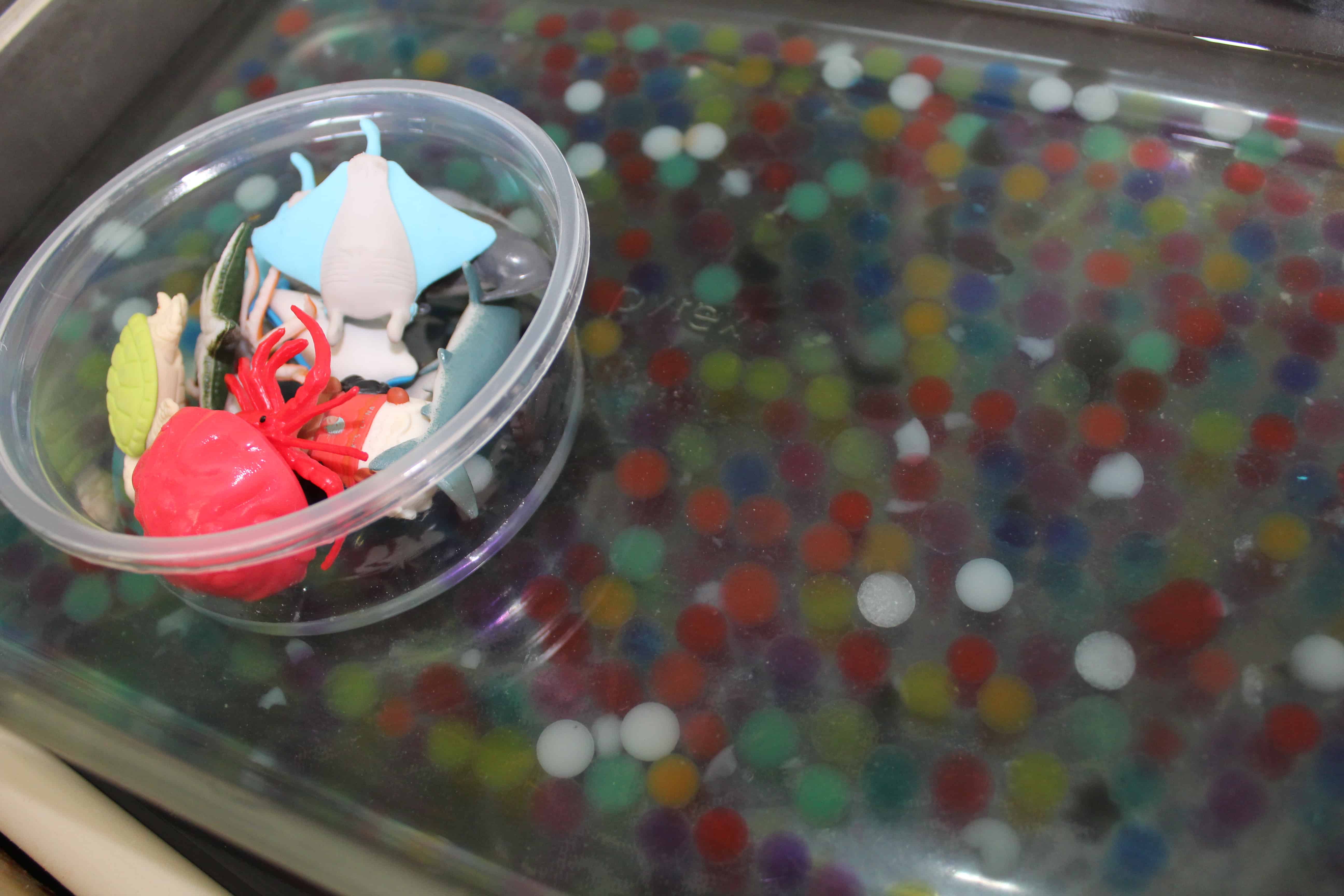 a shallow dish filled with water beads and plastic sea creatures