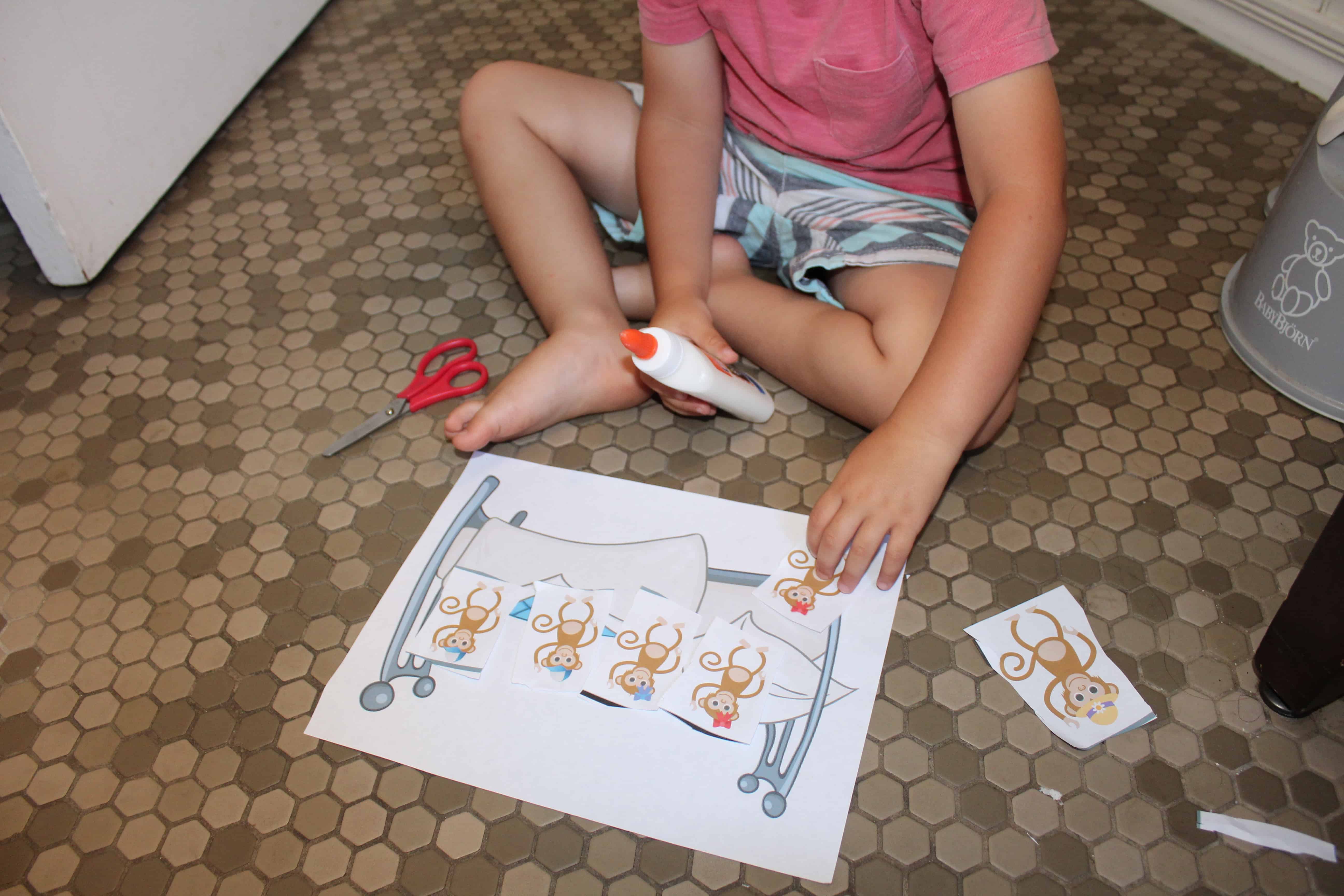 a toddler gluing 5 little monkeys onto a paper bed