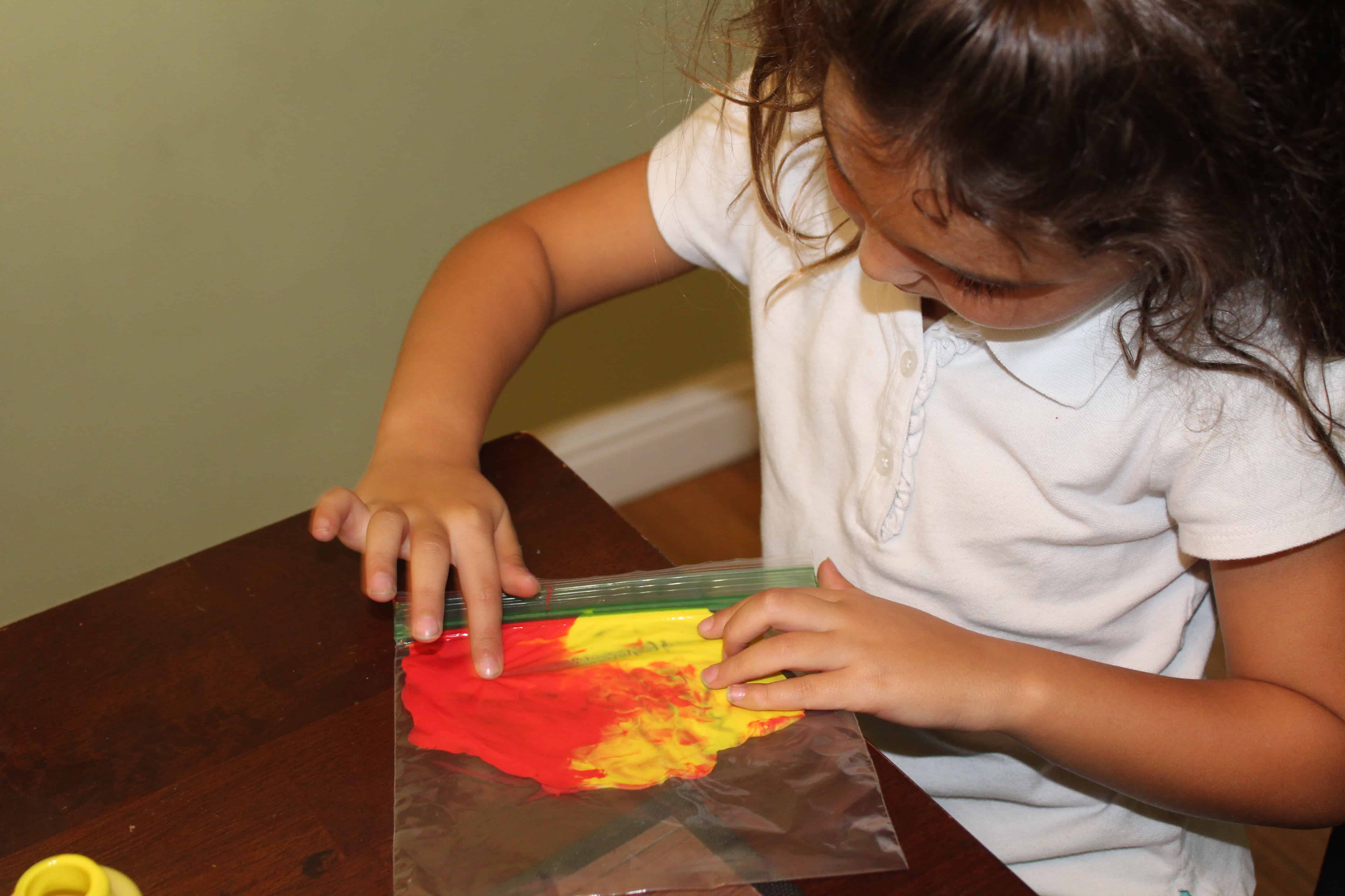 little girl mixing paint colors in a ziploc bag