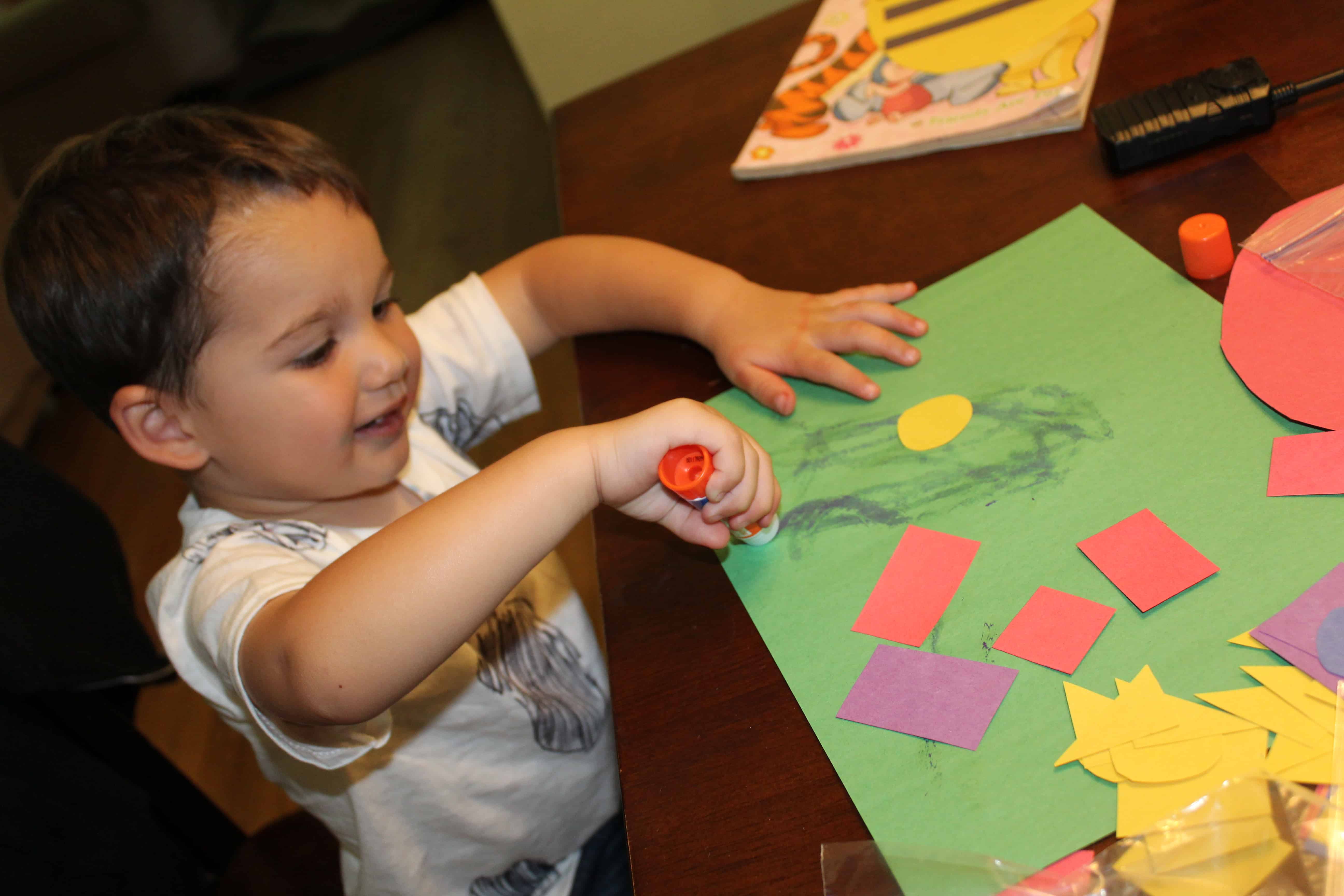 preschooler gluing construction paper shapes onto paper