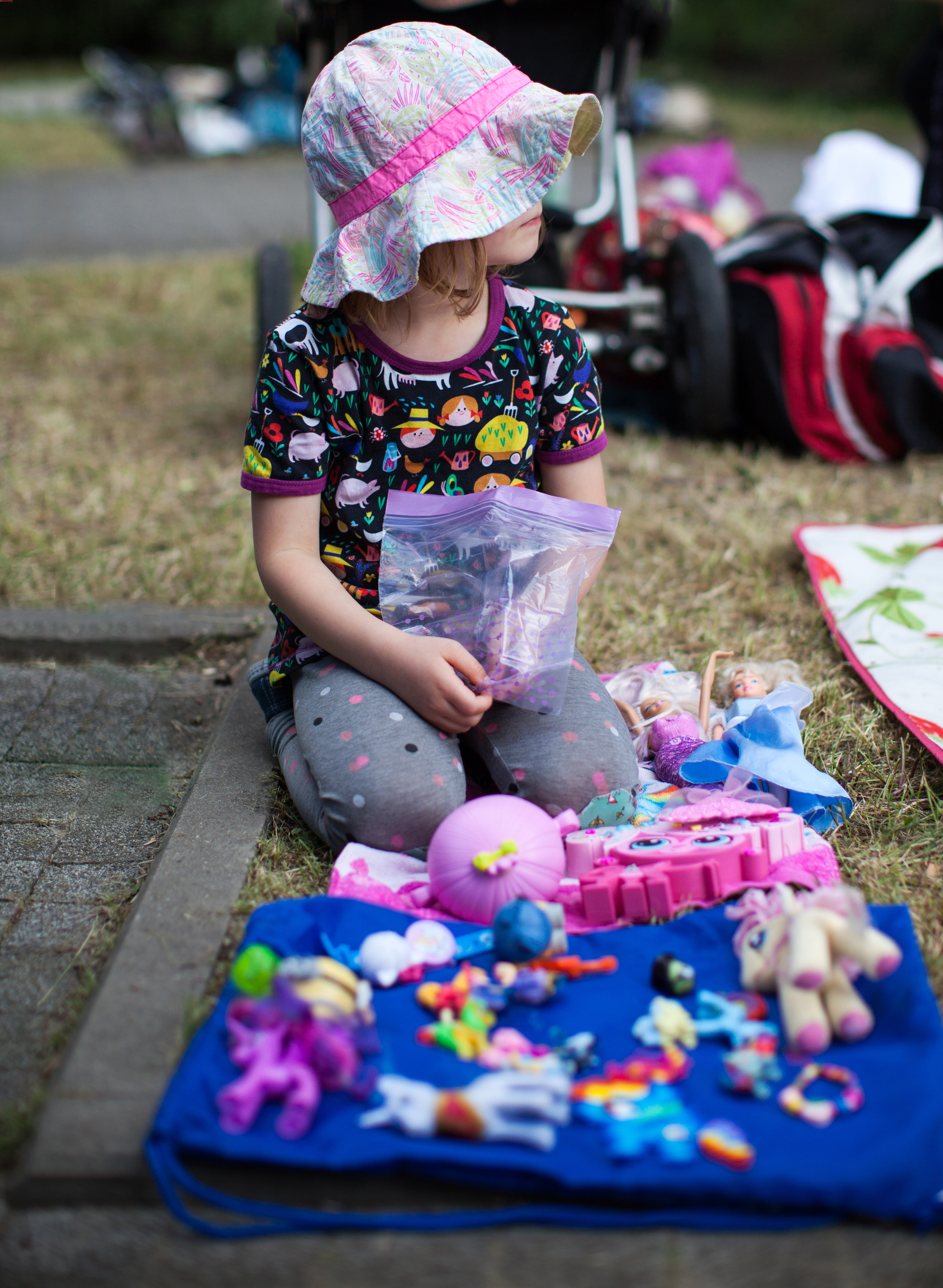 Child sitting in front of a blanket with toys arranged for a garage sale.