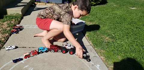 little boy playing with cars outside