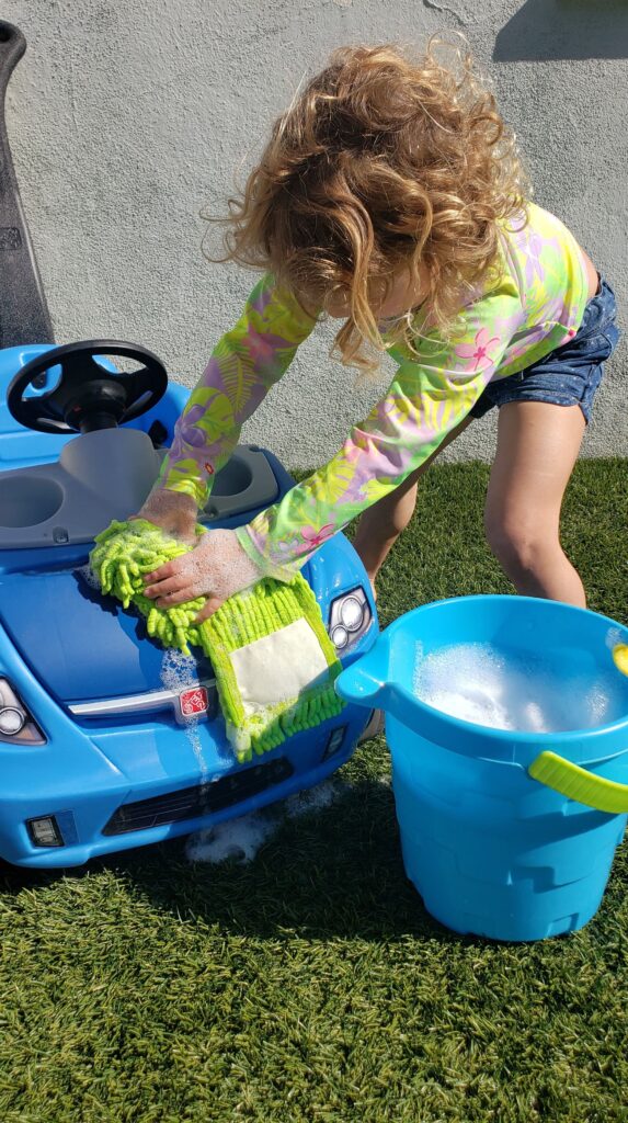 Little girl washing ride on toy car