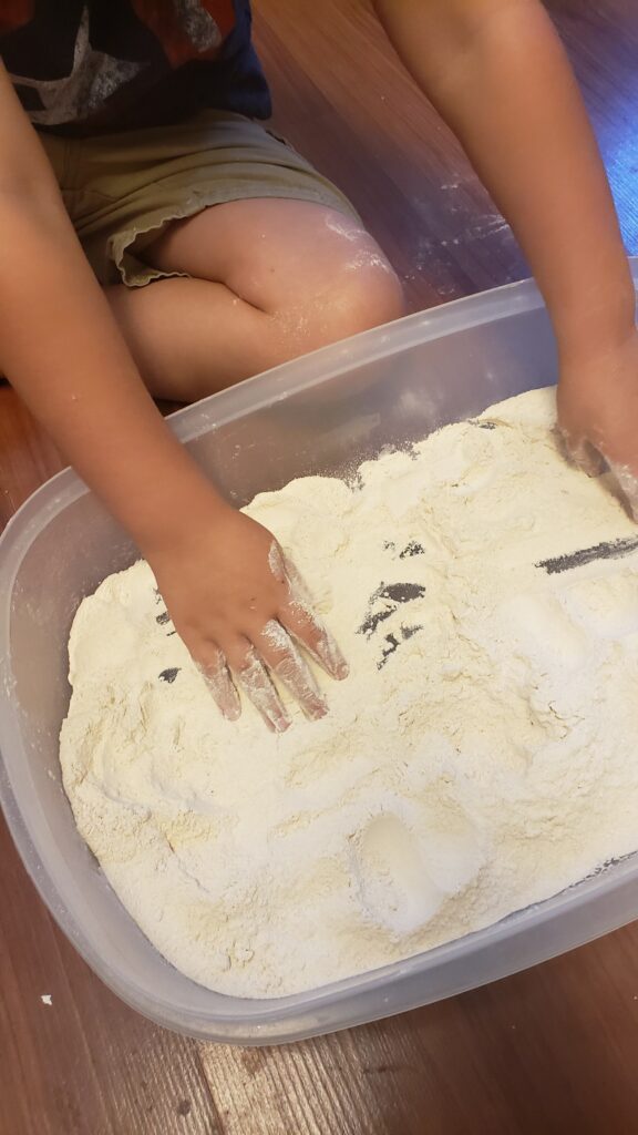 toddler playing with flour sensory bin